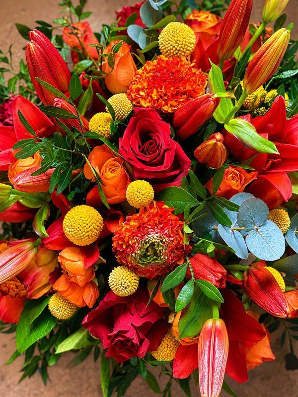 Bouquet tons chauds, roses rouges, lys orange, craspedia et eucalyptus