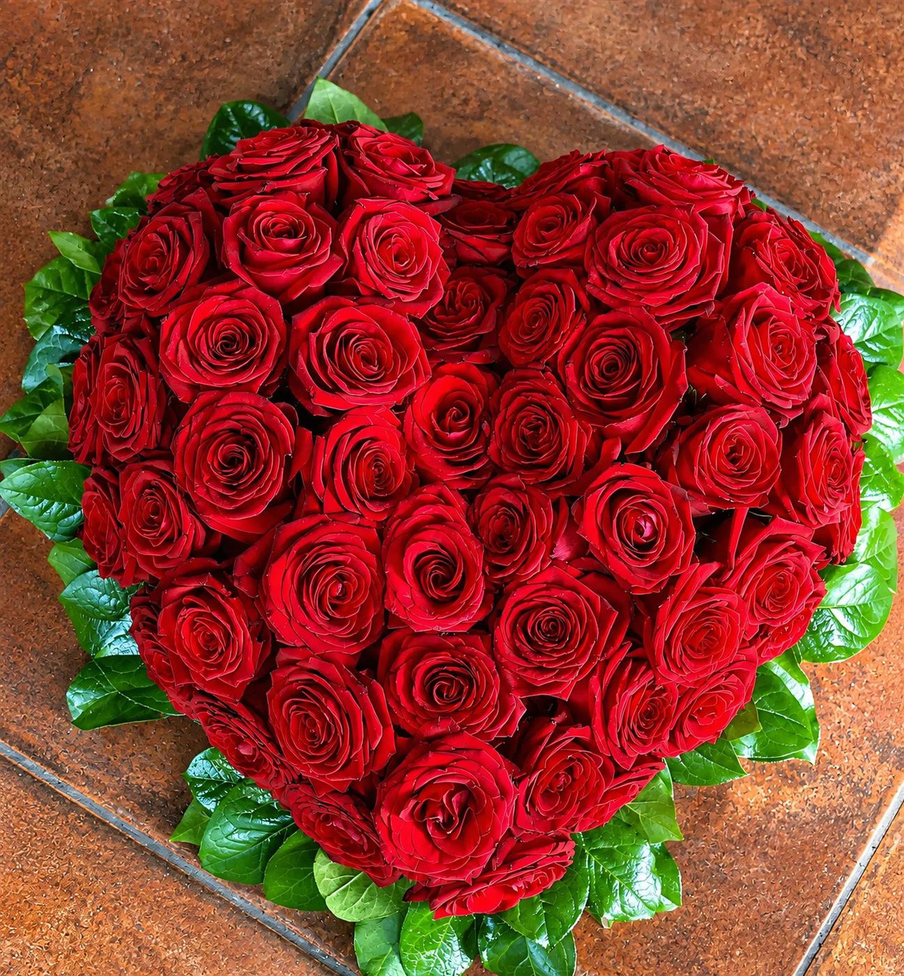 Composition en forme de cœur, roses rouges et feuillage vert pour grands moments