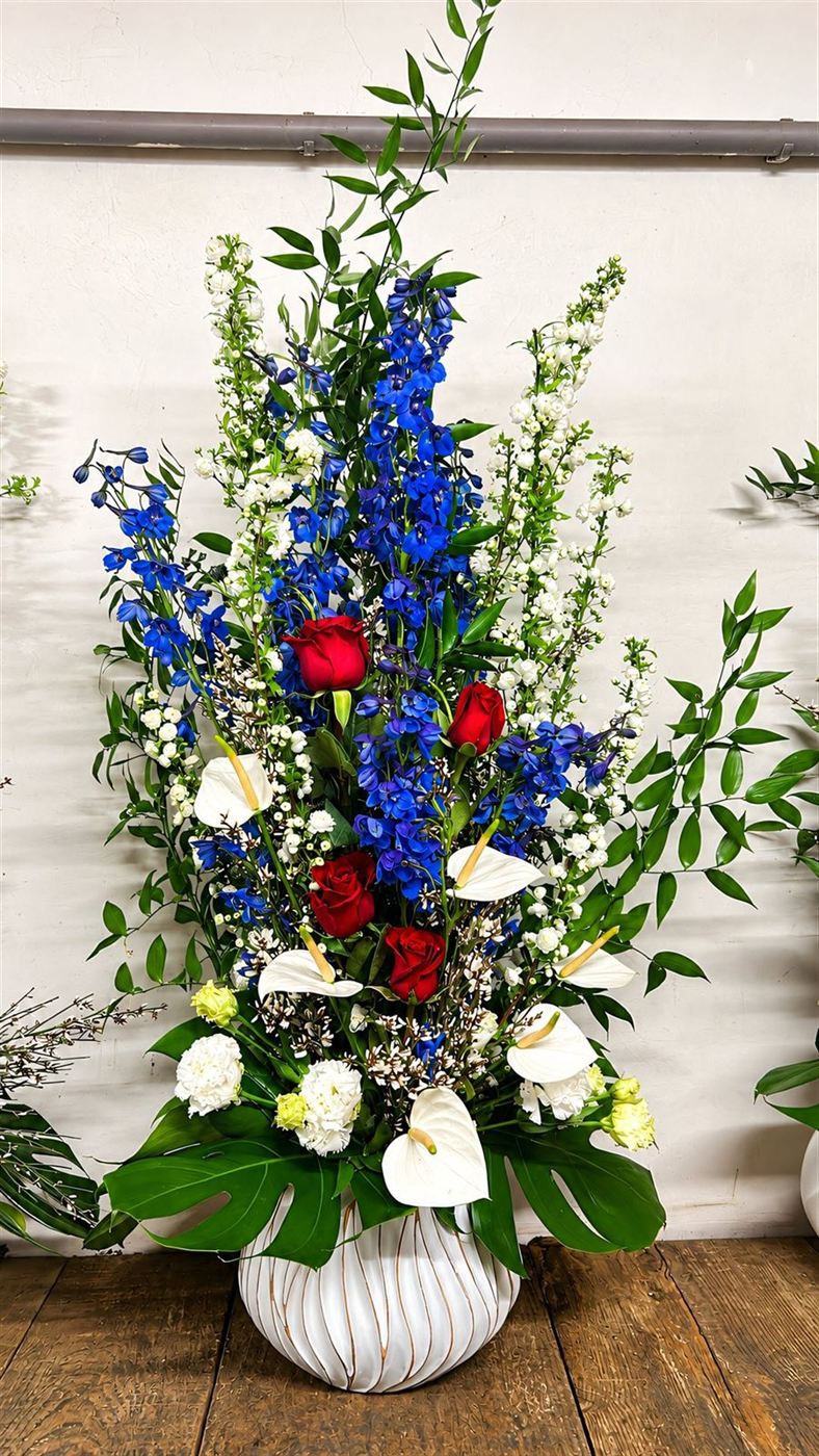Composition sur pied, delphinium bleu, roses rouges et anthuriums blancs