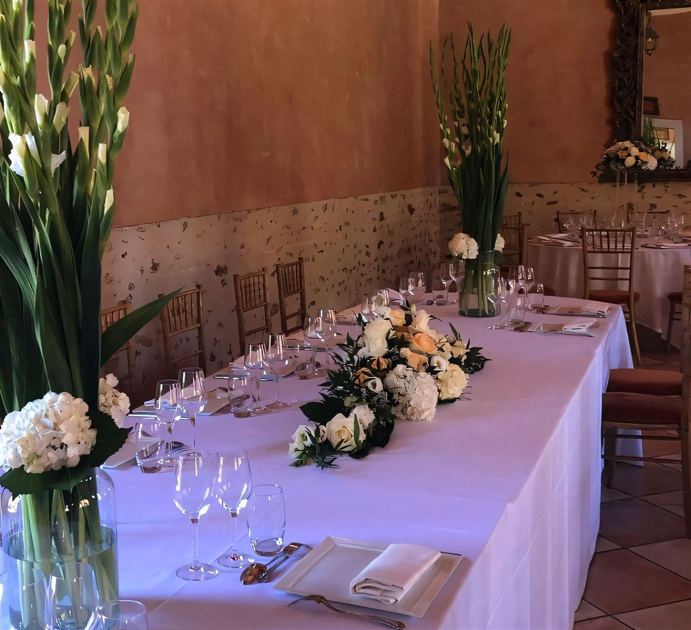 Table de banquet, vases hauts de glaïeuls blancs et centre bas aux roses pêche