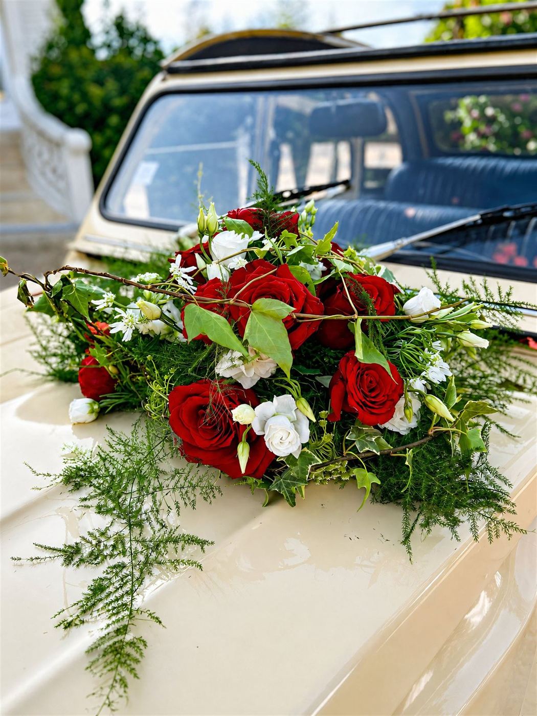 Gerbe posée sur capot, roses rouges, œillets et verdure fine